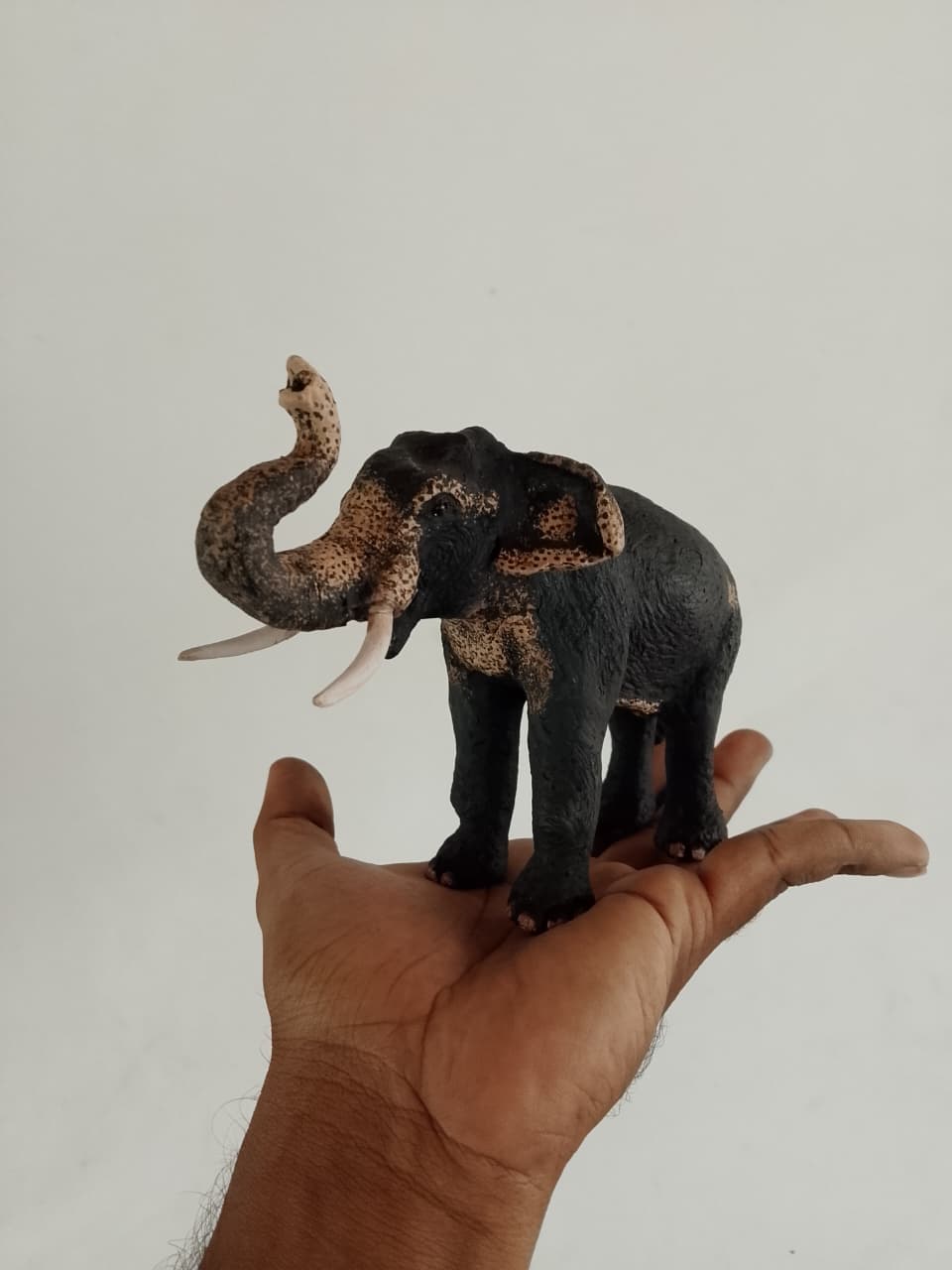 Palm-sized elephant sculpture with its trunk raised, standing on an open hand
