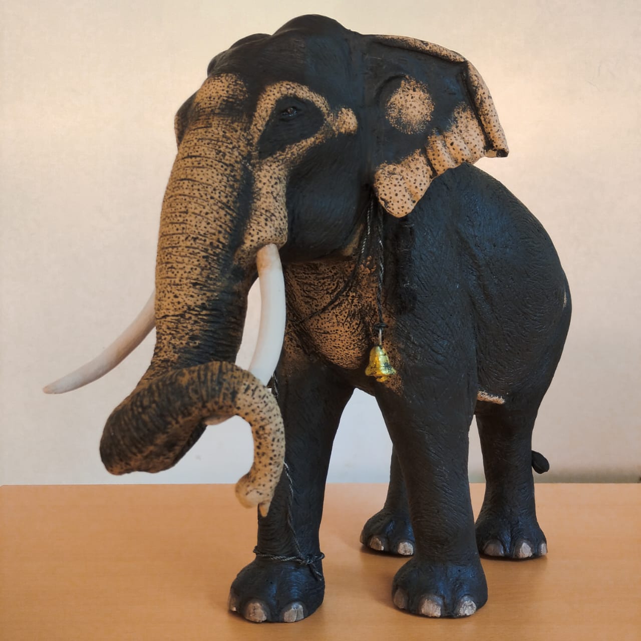 Handmade Sri Lankan tusker sculpture with a curled trunk, pale freckled face and ears, and a small bell