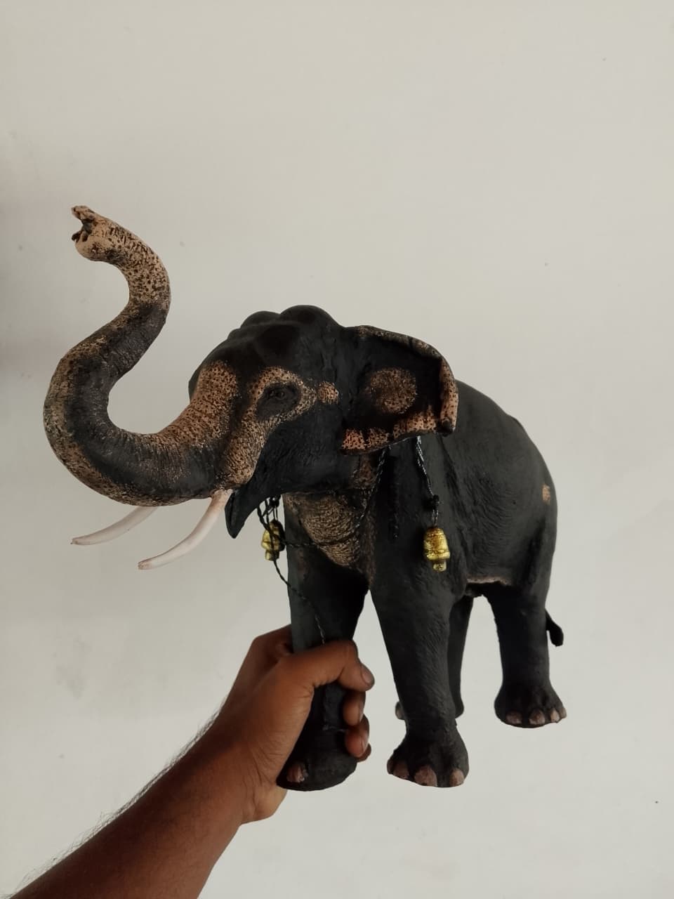 Elephant sculpture with its trunk raised high and two small bells at its throat