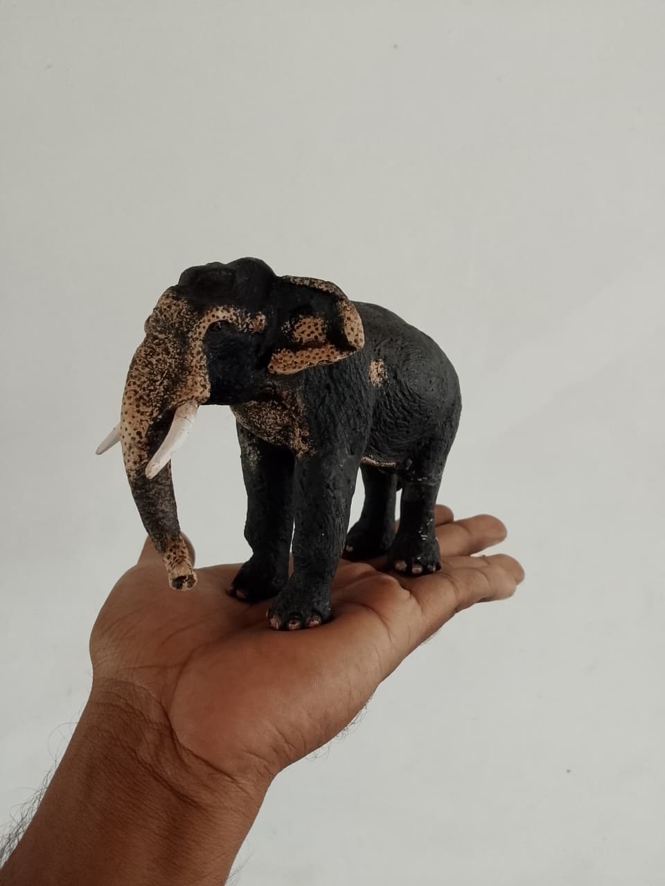 Palm-sized elephant sculpture with its trunk lowered, standing on an open hand